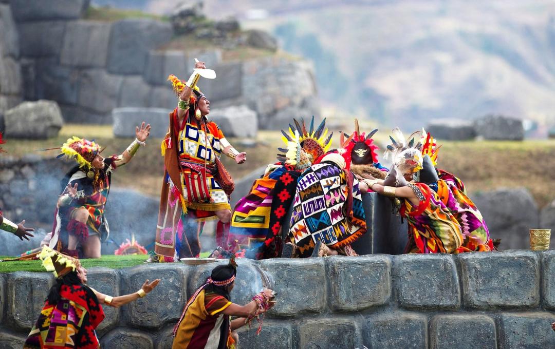 Group of people in colorful Inca costumes performing a dance or ritual on a stone structure, part of Inti Raymi the Festival of the Sun.