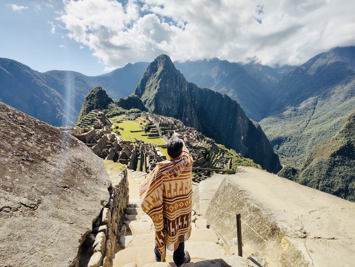 Man with poncho observing Machu Picchu from a height, mountainous landscape, featured in a Tour of Maras, Moray, Ollantaytambo and Machupicchu 2 days and one night