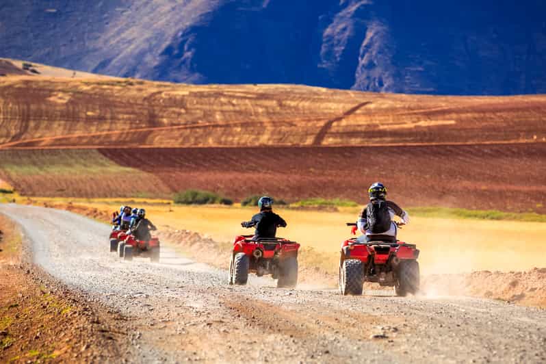 Group of red ATVs on a dirt road, exploring mountainous landscapes and fields, part of the ATV Excursion through the Maras and Moray Salt Mines.